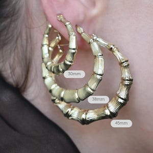 A woman's ear with three nested gold bamboo-style hoop earrings, with white text overlays indicating "30mm", "38mm", and "45mm".