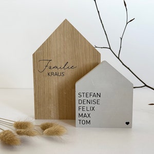 Könnte beinhalten: Ein hölzernes Schild in Form eines Hauses mit dem Text "Familie KRAUS" auf der Vorderseite und den Namen "Stefan, Denise, Felix, Max, Tom" auf der Rückseite.