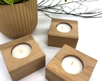May include: Three wooden candle holders with a square base and a circular cutout for a tea light candle. The candle holders are made of natural wood and have a light brown color.