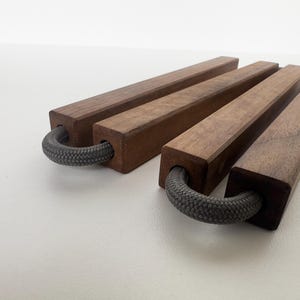 Könnte beinhalten: Vier rechteckige Serviertabletts aus Holz mit dunkelbraunem Finish. Jedes Tablett hat einen grauen Seilgriff. Die Tabletts sind auf einer weißen Oberfläche angeordnet.