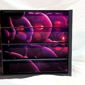 May include: A black, multi-compartment storage unit featuring a purple and pink graphic of cartoon characters with glowing red eyes. The image is divided into four horizontal sections.