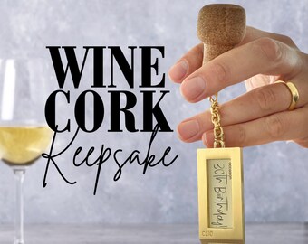 Op de afbeelding: Goudkleurige wijnkurk-sleutelhanger met een ketting en een rechthoekig label met de tekst "gelegenheid: 30e verjaardag! CLIO".