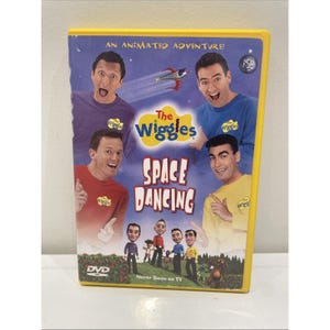 Puede incluir: Una caja de DVD amarilla con el título "The Wiggles Space Dancing". La portada muestra a cuatro personas con camisas coloridas, con las palabras "An Animated Adventure!" en la parte superior. La parte inferior de la caja dice "Never Seen on TV."