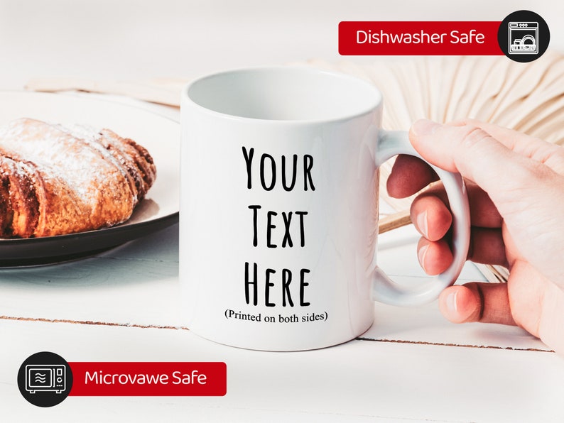 Peut inclure: Mug en c&eacute;ramique blanche avec le texte "YOUR TEXT HERE" imprim&eacute; en noir. Le mug est lavable au lave-vaisselle et au micro-ondes. Un croissant est pos&eacute; sur une assiette en arri&egrave;re-plan.