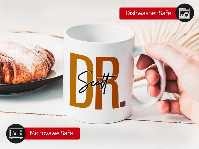 Peut inclure: Une tasse en c&eacute;ramique blanche avec un motif brun et orange qui dit "DR Scott". La tasse est lavable au lave-vaisselle et au micro-ondes.