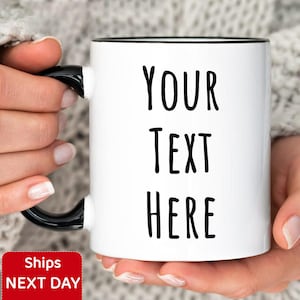 Peut inclure: Mug en c&eacute;ramique blanche avec anse et bord noir, affichant le texte "YOUR TEXT HERE" en noir. Le mug est tenu par une personne portant un pull en tricot blanc. Un autocollant rouge et blanc avec le texte "Ships NEXT DAY" est visible.