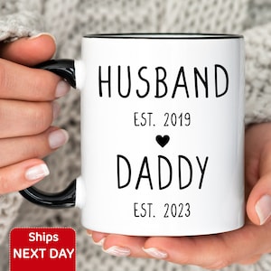 May include: White ceramic coffee mug with black text and a black heart. The text reads "Husband Est. 2019" and "Daddy Est. 2023".