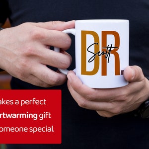 Peut inclure: Une tasse en c&eacute;ramique blanche avec un motif rouge, orange et jaune qui dit "DR. Scott" en lettres noires.