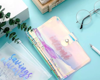 May include: A clear iridescent binder with a snap closure and a silver ring binder mechanism. The binder has the words "wishlist" written on it in a holographic font. The binder is lying on a light blue surface.