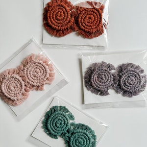 May include: Four pairs of handmade macrame earrings in different colours. The earrings are made with a spiral design and have a fringe around the edges. The colours are rust, pink, grey, and teal.