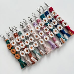 Könnte beinhalten: Ein Set aus zehn bunten gehäkelten Schlüsselanhängern mit Gänseblümchen-Designs. Jeder Schlüsselanhänger hat einen silbernen Schlüsselring und einen Quasten am Ende.