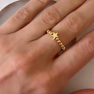 May include: A gold ring with a small star charm. The ring is made of small beads.