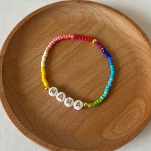 May include: A rainbow beaded bracelet with white letter beads spelling out "MAMA".