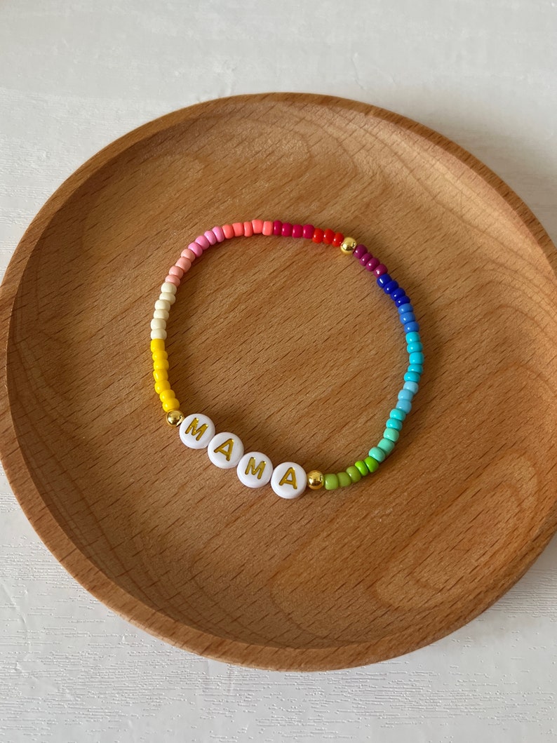 May include: A rainbow beaded bracelet with white letter beads spelling out "MAMA".