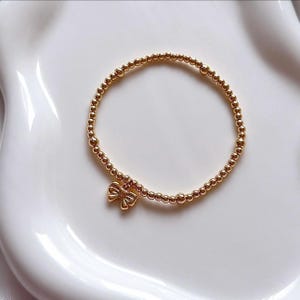 May include: A gold beaded bracelet with a small gold bow charm.