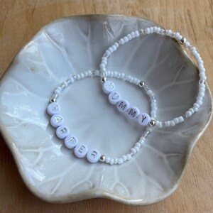 May include: Two white beaded bracelets with silver beads. One bracelet spells "MUMMY" and the other spells "HARPER".