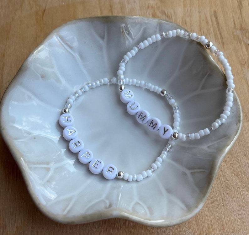 May include: Two white beaded bracelets with silver beads. One bracelet spells "MUMMY" and the other spells "HARPER".