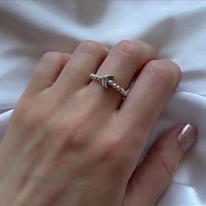 May include: A silver ring with a crescent moon charm and a beaded band.