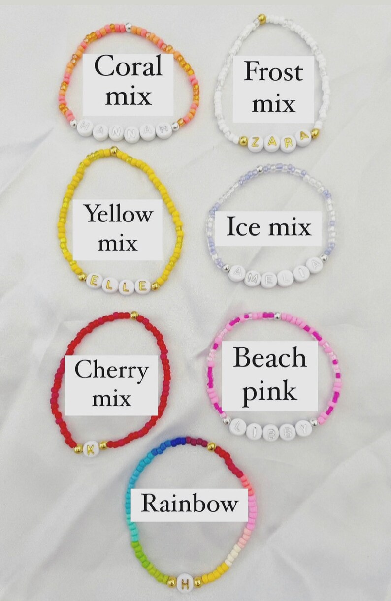 May include: Six colorful beaded bracelets with white letter beads spelling out names. The bracelets are arranged in two rows of three. The top row includes coral, frost, and yellow mix bracelets. The bottom row includes ice mix, cherry mix, and beach pink bracelets. The bottom row also includes a rainbow bracelet.