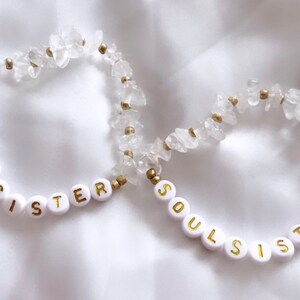 May include: Two white bracelets with gold beads and white letter beads spelling "Soul Sister".