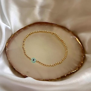 May include: A gold beaded bracelet with a blue and green evil eye charm.