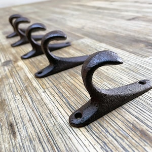 Könnte beinhalten: Fünf rustikale schwarze Gusseisenhaken, die auf einer Holzoberfläche montiert sind. Die Haken sind gebogen und haben eine patinierte Oberfläche.