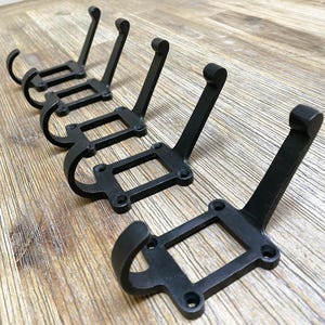 May include: Five black metal hooks with a rectangular base. The hooks are arranged in a row, with the hooks facing the same direction.