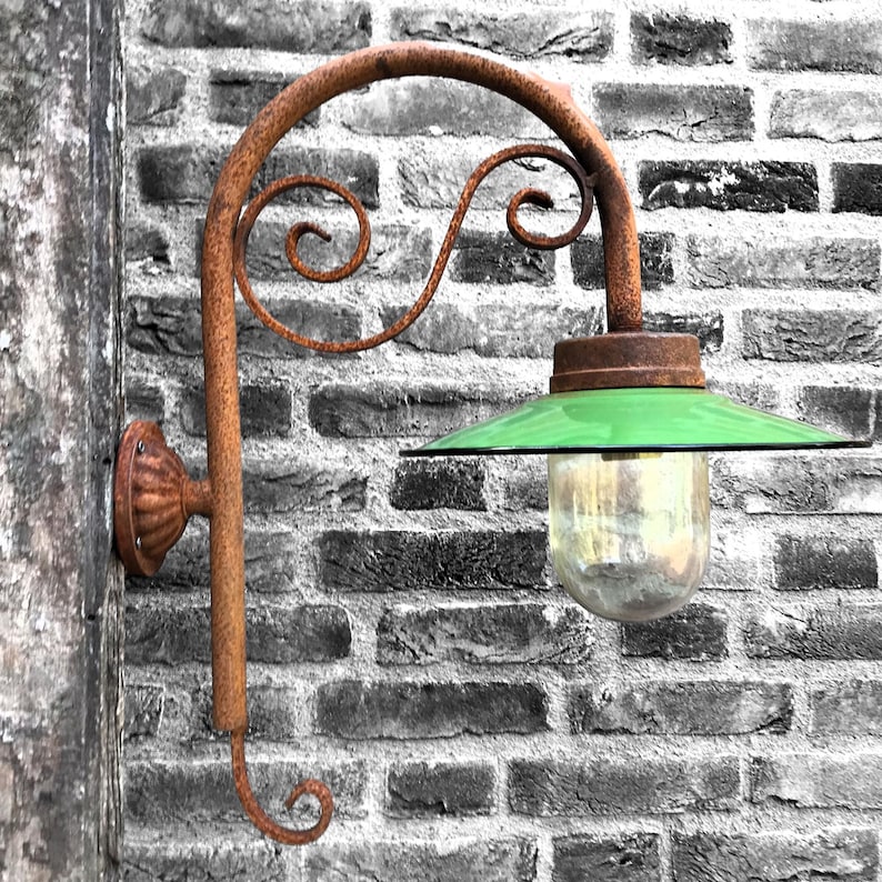 May include: A rusty metal wall-mounted lamp with a green glass shade and a clear glass globe. The lamp is mounted on a brick wall.