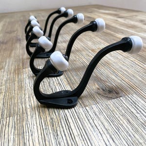 May include: A row of black metal hooks with white ceramic knobs. The hooks are arranged in a line on a wooden surface.