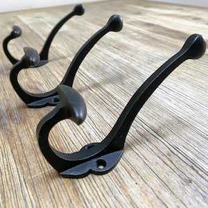 Könnte beinhalten: Drei schwarze Metallhaken mit gebogenem Design. Die Haken sind auf einer Holzoberfläche montiert.