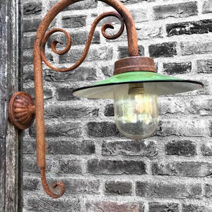 May include: A rusty metal outdoor light fixture with a green glass shade and a clear glass bulb. The light is mounted on a brick wall.