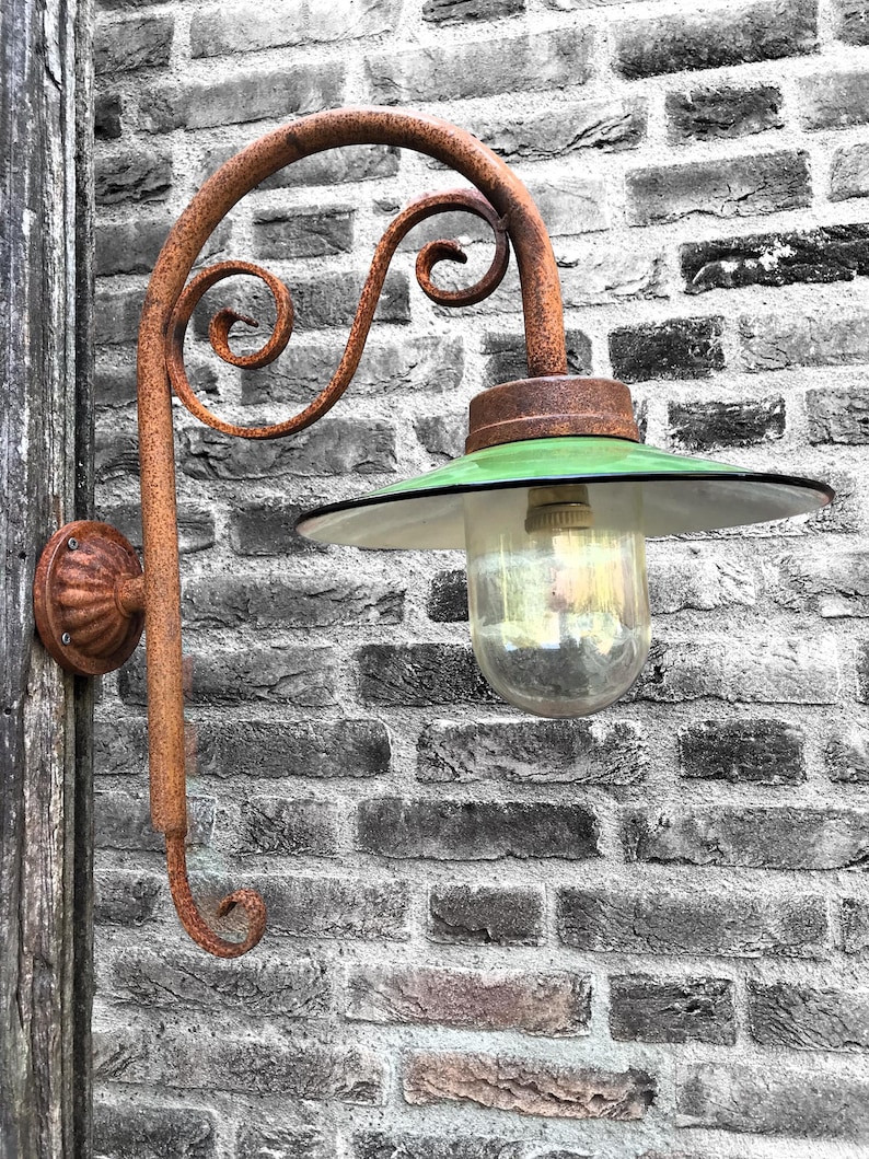 May include: A rusty metal outdoor light fixture with a green glass shade and a clear glass bulb. The light is mounted on a brick wall.