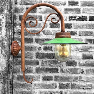 May include: A rusty metal wall sconce with a green glass shade and a clear glass bulb. The sconce is mounted on a brick wall.