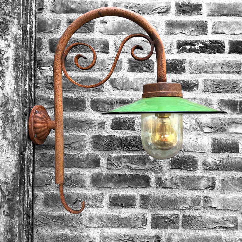 May include: A rusty metal wall sconce with a green glass shade and a clear glass bulb. The sconce is mounted on a brick wall.