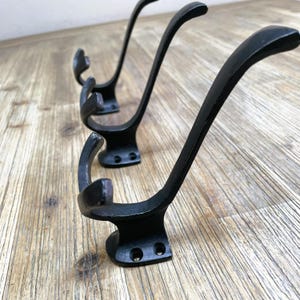 Op de afbeelding: Drie zwarte metalen haken met een gebogen ontwerp. De haken zijn gemonteerd op een houten oppervlak.