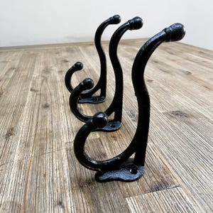 May include: Four black metal hooks with a curved design. The hooks are arranged in a row on a wooden surface.