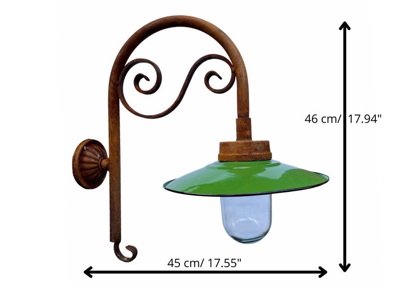 May include: Rustic wall-mounted light fixture with a green metal shade and a clear glass globe. The fixture has a decorative, scrolled metal arm and measures 17.94 inches tall and 17.55 inches wide.