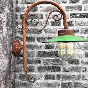 Könnte beinhalten: Eine rostige Wandleuchte aus Metall mit einem grünen Glasschirm und einer klaren Glühbirne. Die Leuchte ist an einer Backsteinwand montiert.