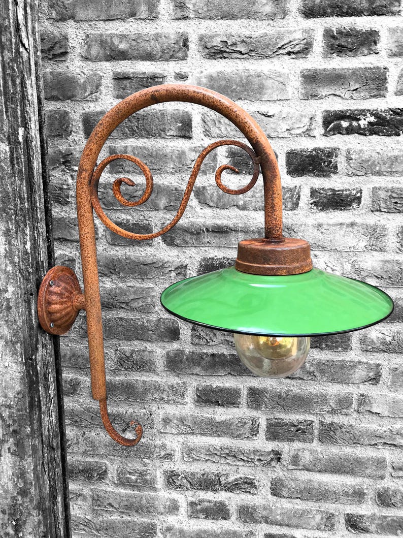 May include: A rusty metal wall-mounted light fixture with a green glass shade and a clear glass bulb. The fixture has a decorative scroll design.