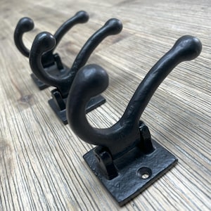 Op de afbeelding: Drie zwarte metalen haken met een vierkante basis. De haken zijn ontworpen met een dubbele bocht om items aan op te hangen.