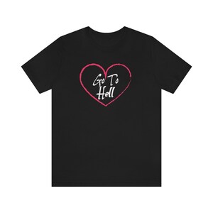 以下が含まれることがあります： ピンクのハートと白い文字「Go To Hell」が書かれた黒いTシャツ