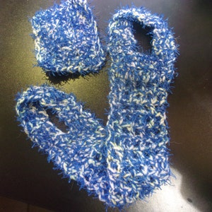 Pode incluir: Uma echarpe de crochê azul e branca com uma textura felpuda. A echarpe é feita de fio e tem uma forma longa e fina.