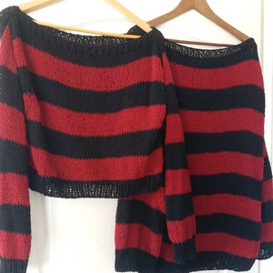 May include: A red and black striped knitted sweater and skirt set. The sweater is a cropped style with long sleeves and a wide neckline. The skirt is a midi length with a straight silhouette.