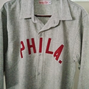 May include: Gray baseball jersey with red embroidered lettering that reads "PHILA".