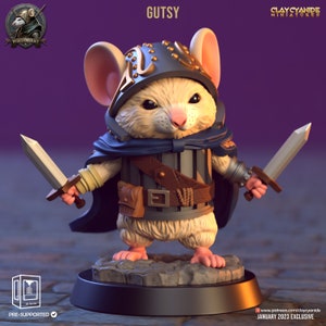 May include: A small, white, mouse-like creature wearing a blue cape and a helmet with gold accents. The creature is holding two swords, one in each hand. The creature is standing on a black base with a rocky texture. The text "GUTSY" is written in white letters above the creature. The text "CLAY CYANIDE MINIATURES" is written in white letters above the text "GUTSY". The text "PRE-SUPPORTED" is written in white letters below the creature. The text "JANUARY 2023 EXCLUSIVE" is written in white letters below the base.