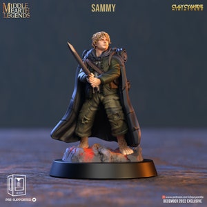 May include: A painted miniature figurine of a character from the Lord of the Rings, holding a sword and wearing a cloak. The figurine is standing on a rocky base. The text "SAMMY" is visible above the figurine.