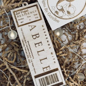 May include: A wooden ticket stub with the text "Las Vegas Residency" and "Abelle" with the date "Saturday, February 25th, 2023" and the location "THE COLOSSEUM AT CAESARS PALACE - Las Vegas, Nevada".