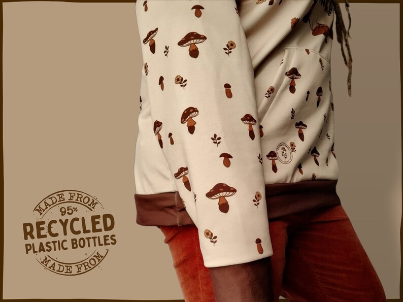 May include: A cream-colored hoodie with a brown mushroom print. The hoodie has a brown drawstring and a brown pocket. The hoodie is made from 95% recycled plastic bottles. The text "MADE FROM 95% RECYCLED PLASTIC BOTTLES MADE FROM" is printed on a brown circle.