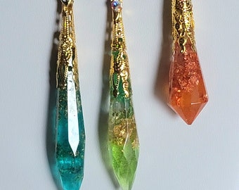 May include: Three pendant necklaces with gold-colored filigree caps and silver chains. The pendants are teardrop-shaped, with teal, green, and orange resin. Each pendant has gold leaf accents.
