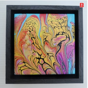 May include: Abstract art piece in a black frame. The artwork features a vibrant mix of colors, including gold, yellow, orange, pink, and blue, creating a fluid, marbled effect. The painting is square and set against a white background.